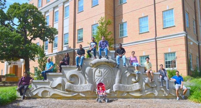 Bioinformatics team posing for a photo on the Biology and Chemistry monument on campus with a stroller